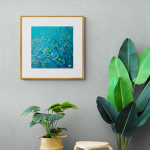 Framed turquoise blue print of "Blennies in the Coral" hanging above two plants